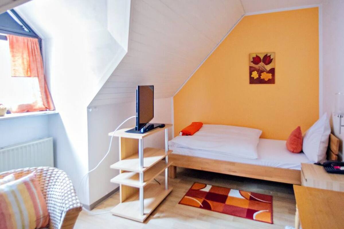 Um quarto com cama em mezzanine, televisão em suporte, janela com cortinas e um quadro na parede.