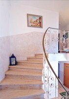 Una escalera de madera con barandilla de metal, un cuadro enmarcado en la pared y un farol a la izquierda.