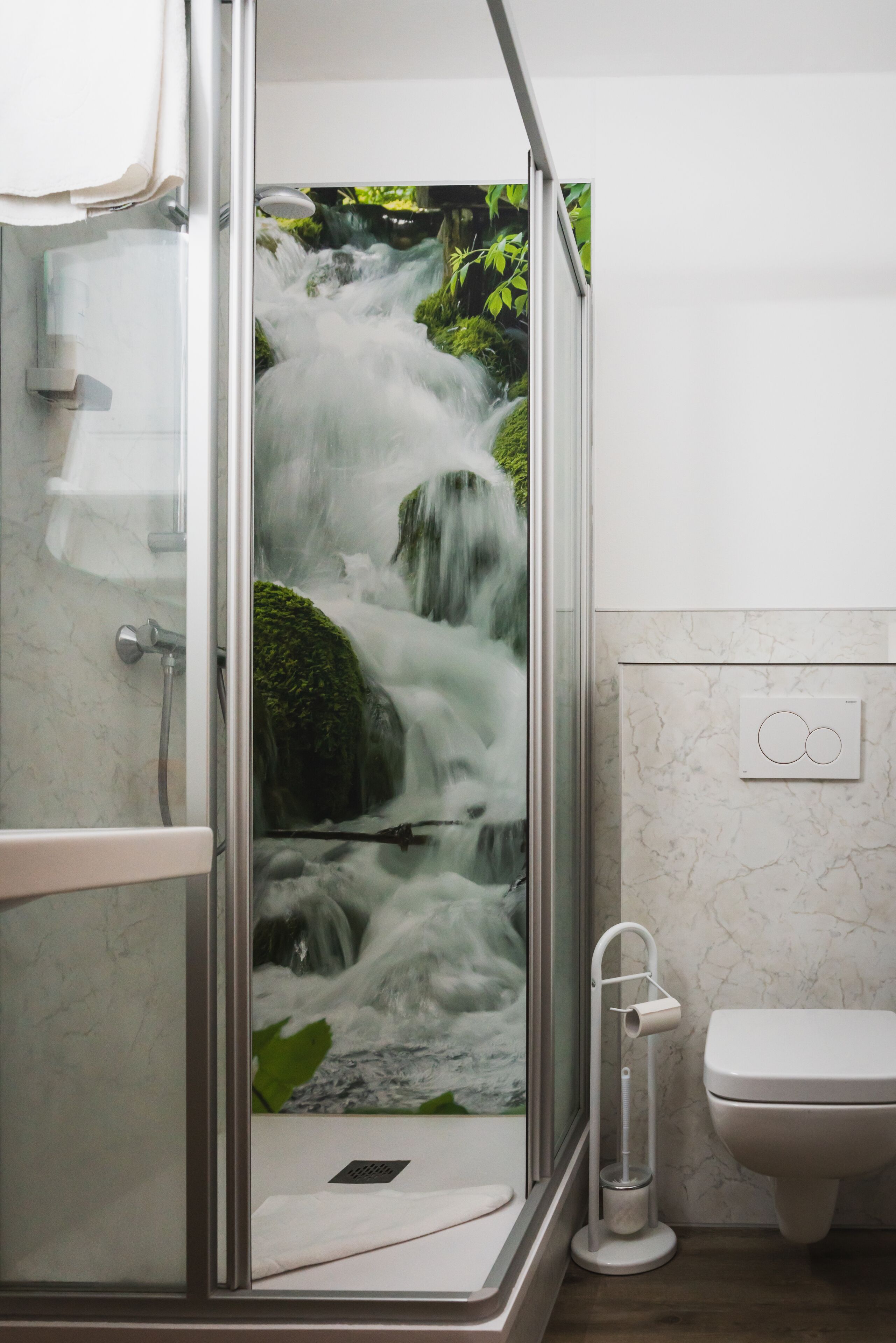 A bathroom with a glass shower enclosure, a toilet, and a marble wall.