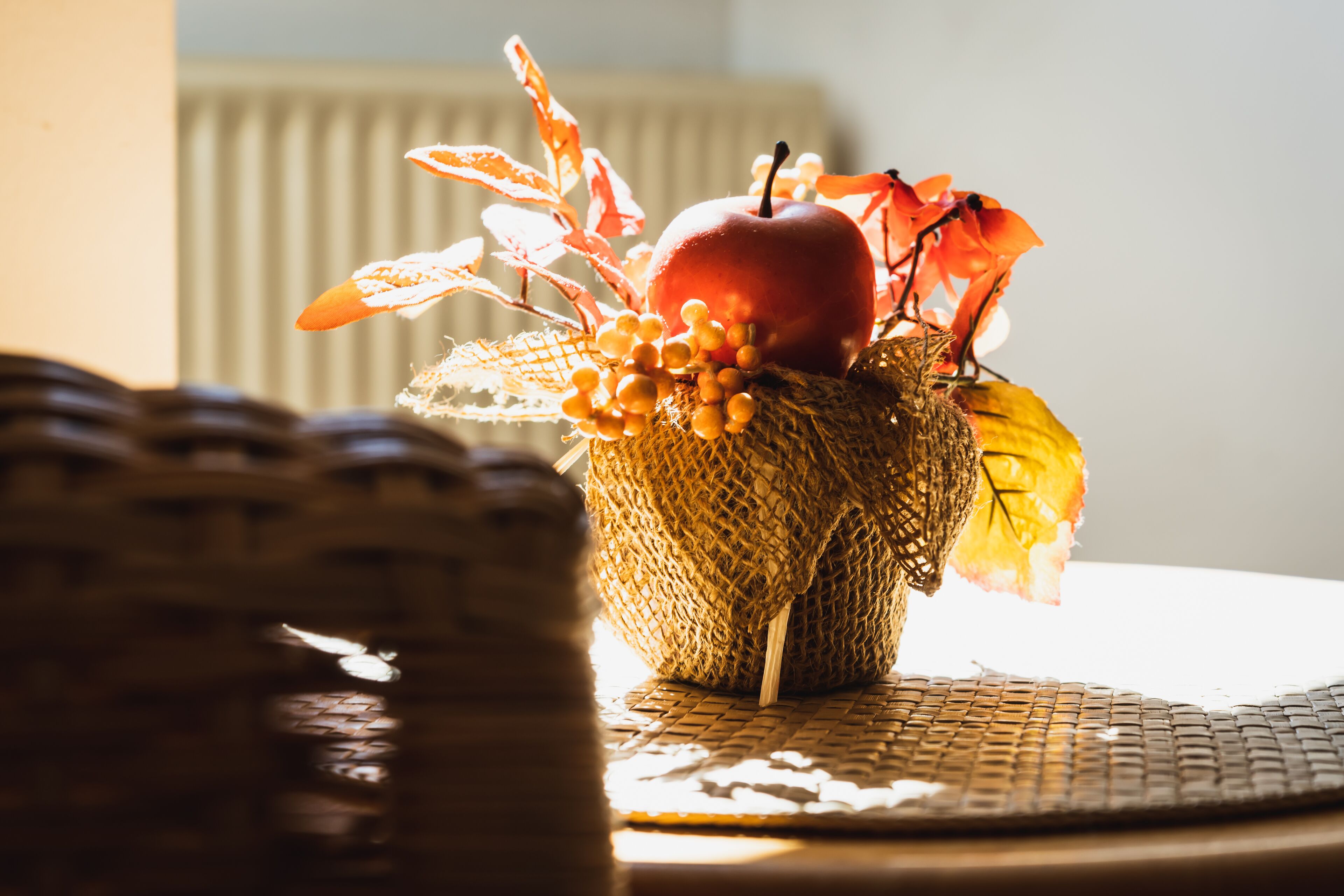 A wicker basket with a red apple, orange leaves, and yellow berries on a woven mat.
