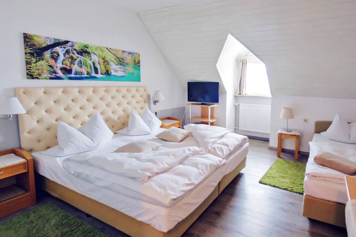 Um quarto espaçoso com uma cama grande, uma televisão e uma pintura de uma cachoeira.