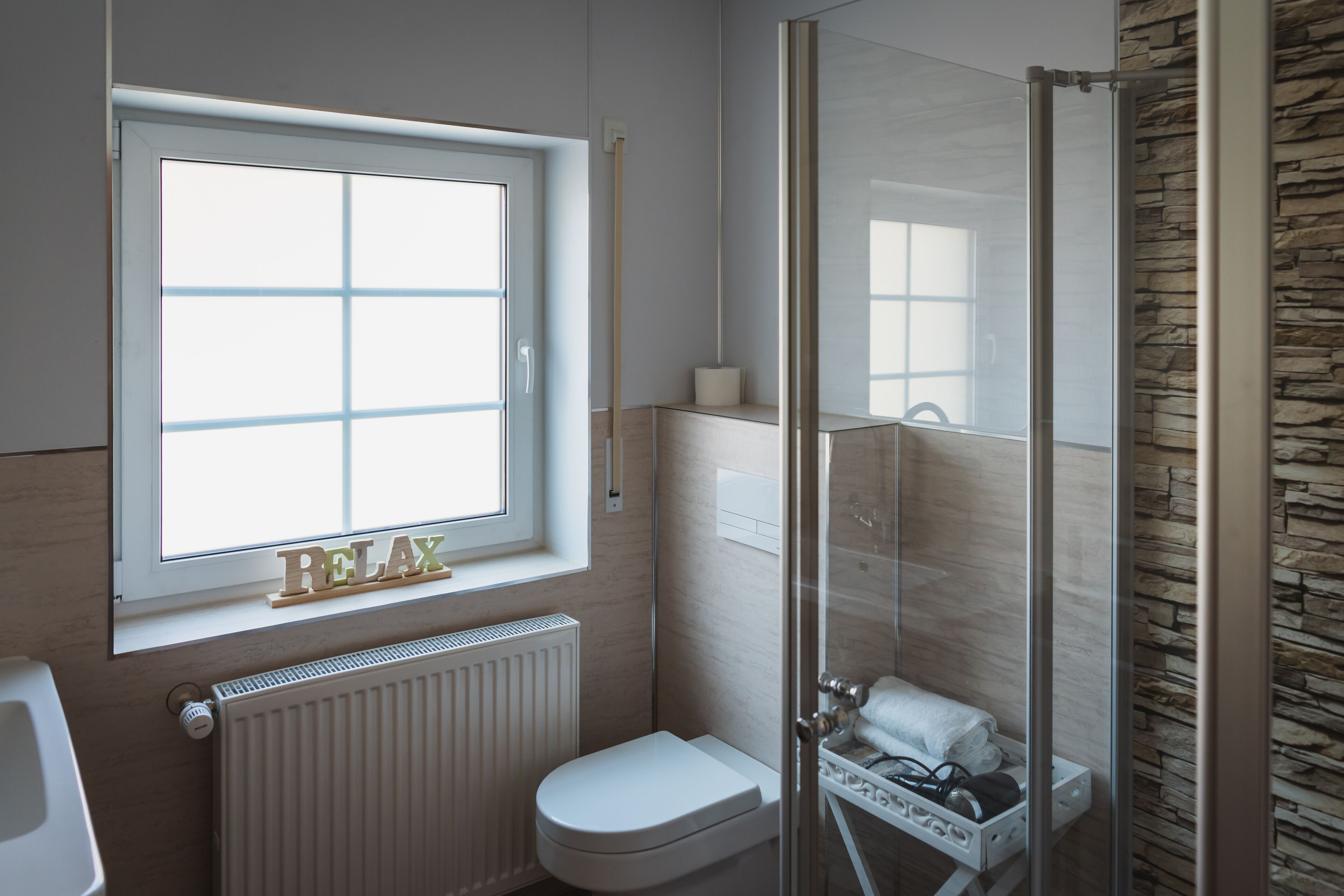 A modern bathroom with a window, a toilet, a shower, and a towel rack.