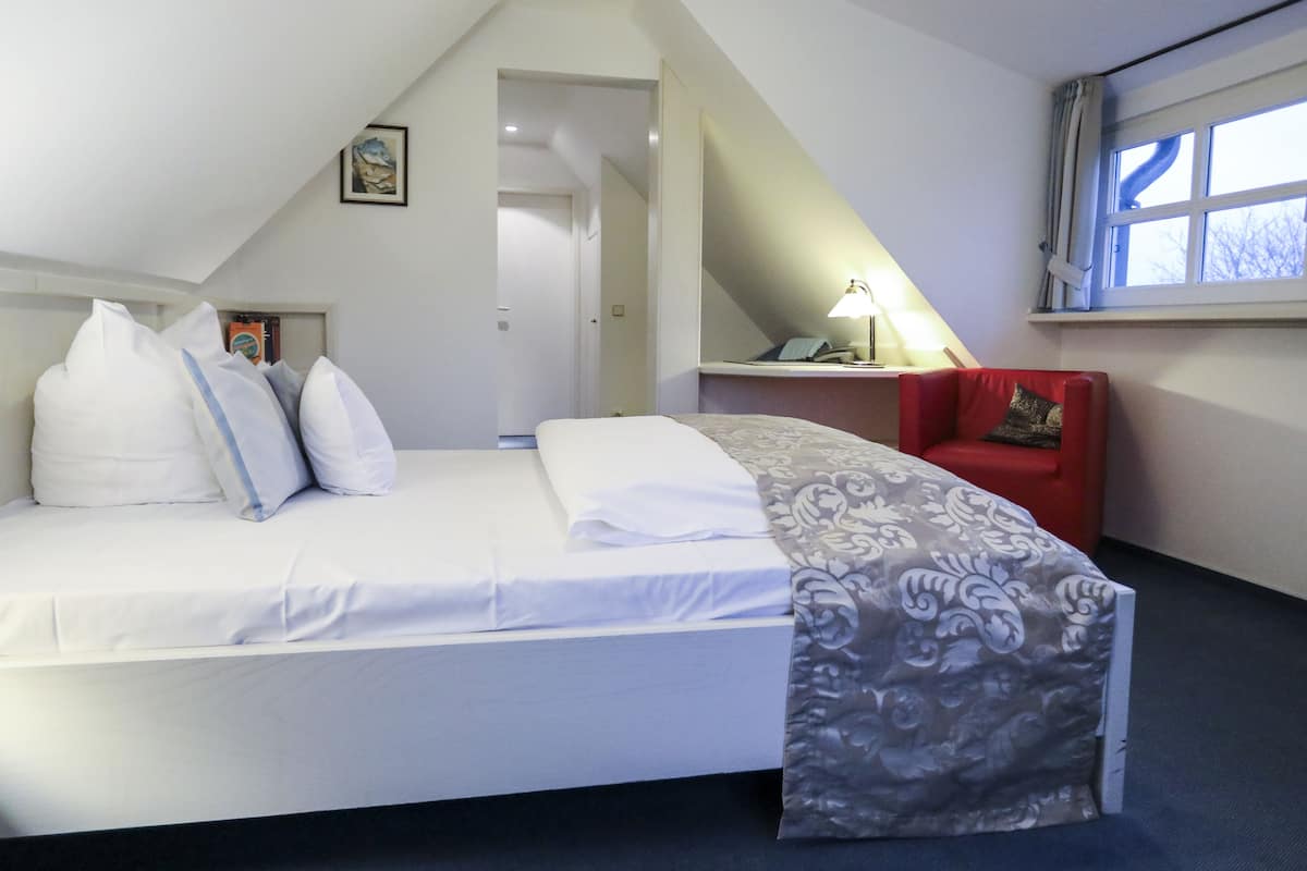 Une chambre à coucher avec un lit, une chaise rouge, un bureau avec une lampe et une fenêtre.