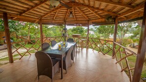 A covered outdoor dining area with a table and chairs, surrounded by a wooden fence and lush greenery. - Hilltop Pool and Villa (Puerto Princesa)