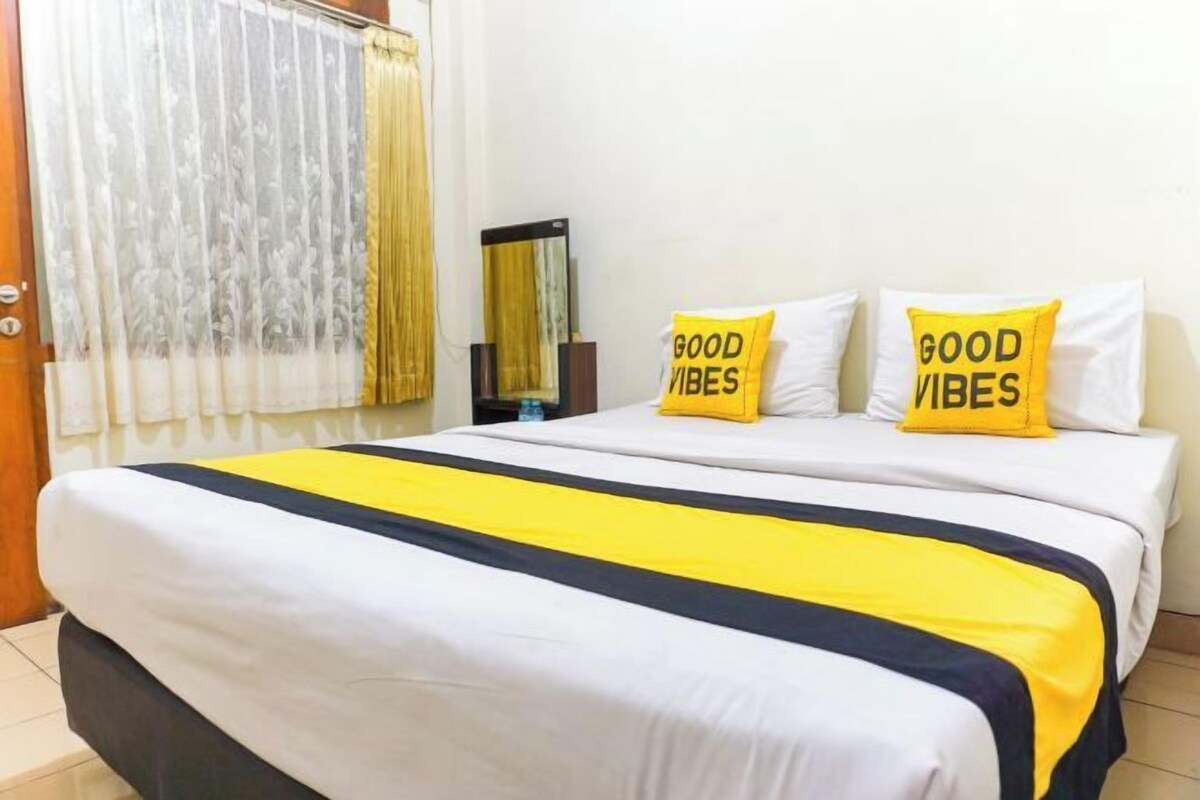 A hotel room with a bed, two pillows with 'GOOD VIBES' text, a bedside table, and a window with curtains.