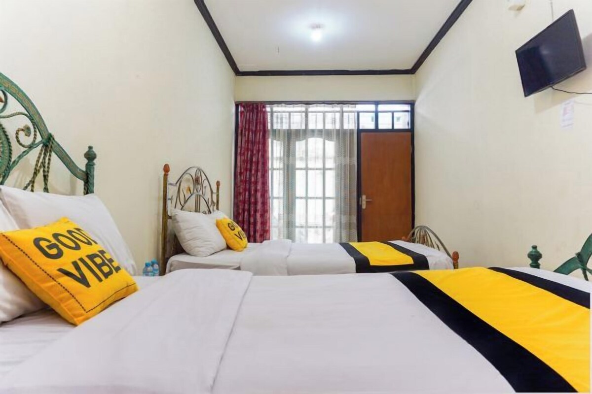 A hotel room with two beds, a television on the wall, and a window with curtains.