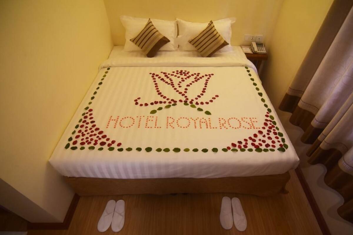 A hotel room with a bed, pillows, a bedside table with a phone, and a decorative bedspread with the hotel's name.