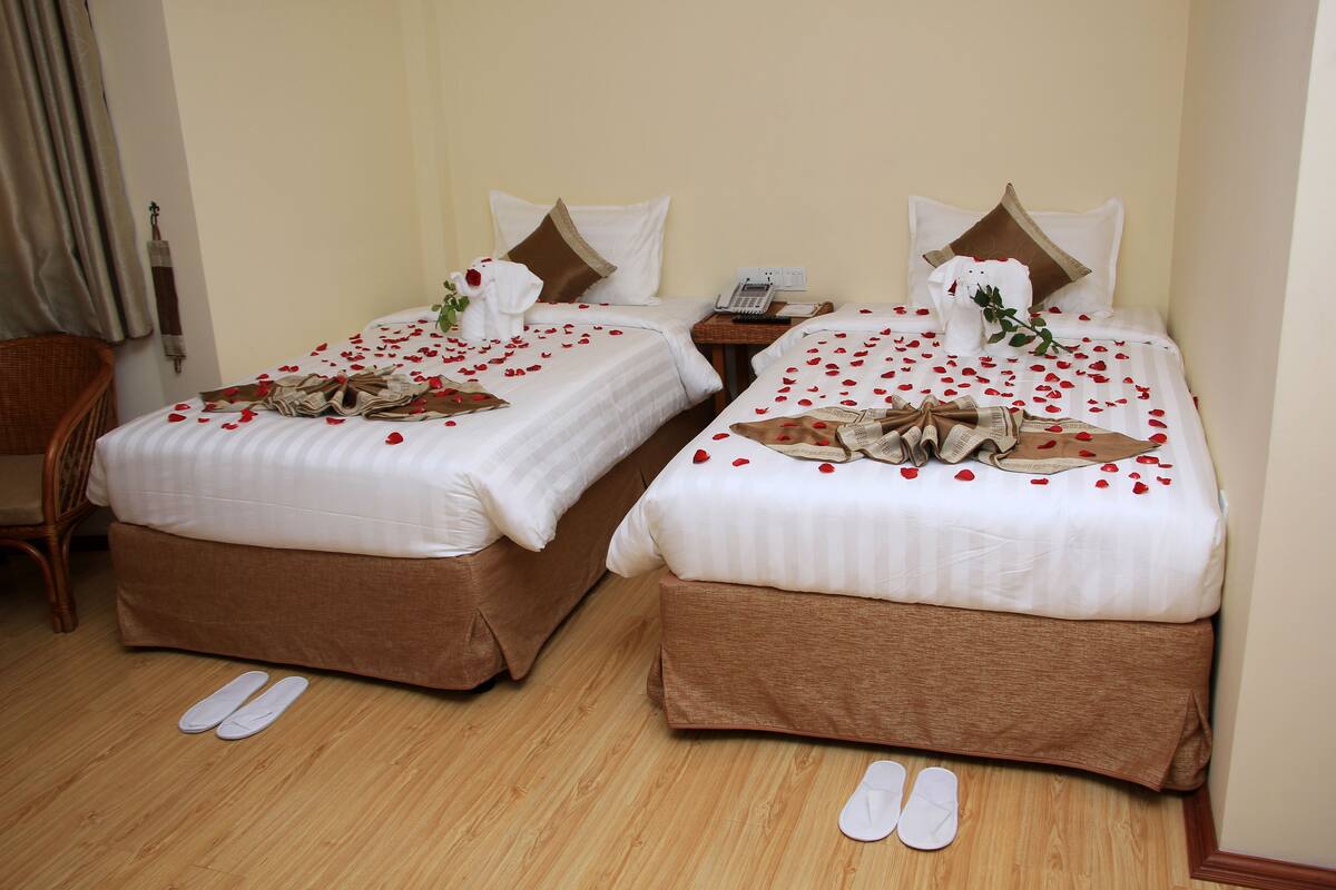 Two beds with white and brown bedding, a wooden floor, and a chair.