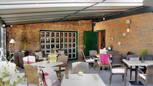 Un patio al aire libre con paredes de ladrillo, puertas verdes, muebles de mimbre y mesas dispuestas para comer.