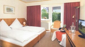 Habitación de hotel con una cama grande, un escritorio con ordenador, una silla y una ventana con cortinas.