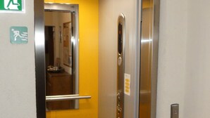 An elevator with a metallic door, a green emergency exit sign, and a yellow wall. - Hotel Krone (Deckenpfronn)