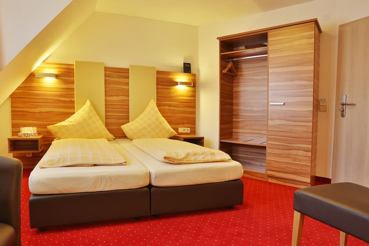 A bedroom with a double bed, wooden headboard, bedside tables, a red carpet, and a wardrobe.