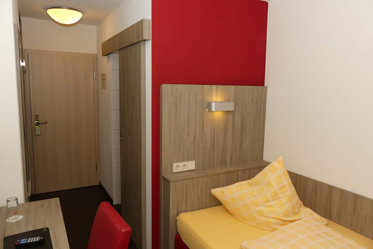 A hotel room with a bed, a desk with a chair, a red wall, and a wooden headboard.