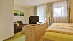 A hotel room with a bed, a TV on a wooden desk, a sofa, and a painting on the wall. - Hotel Krone (Deckenpfronn)