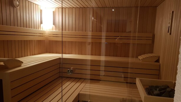 A sauna with wooden benches, a glass door, and a small table with a bowl. - Hotel Krone (Deckenpfronn)