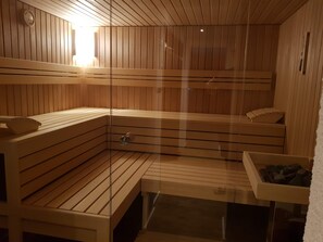 Una sauna con bancos de madera, una puerta de cristal y una pequeña mesa con un cuenco.