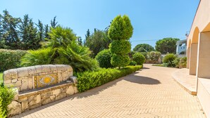 A paved pathway leading to a building with a stone wall and a decorative tile. - Villa Arenella con Piscina by Wonderful Italy (Syracuse)