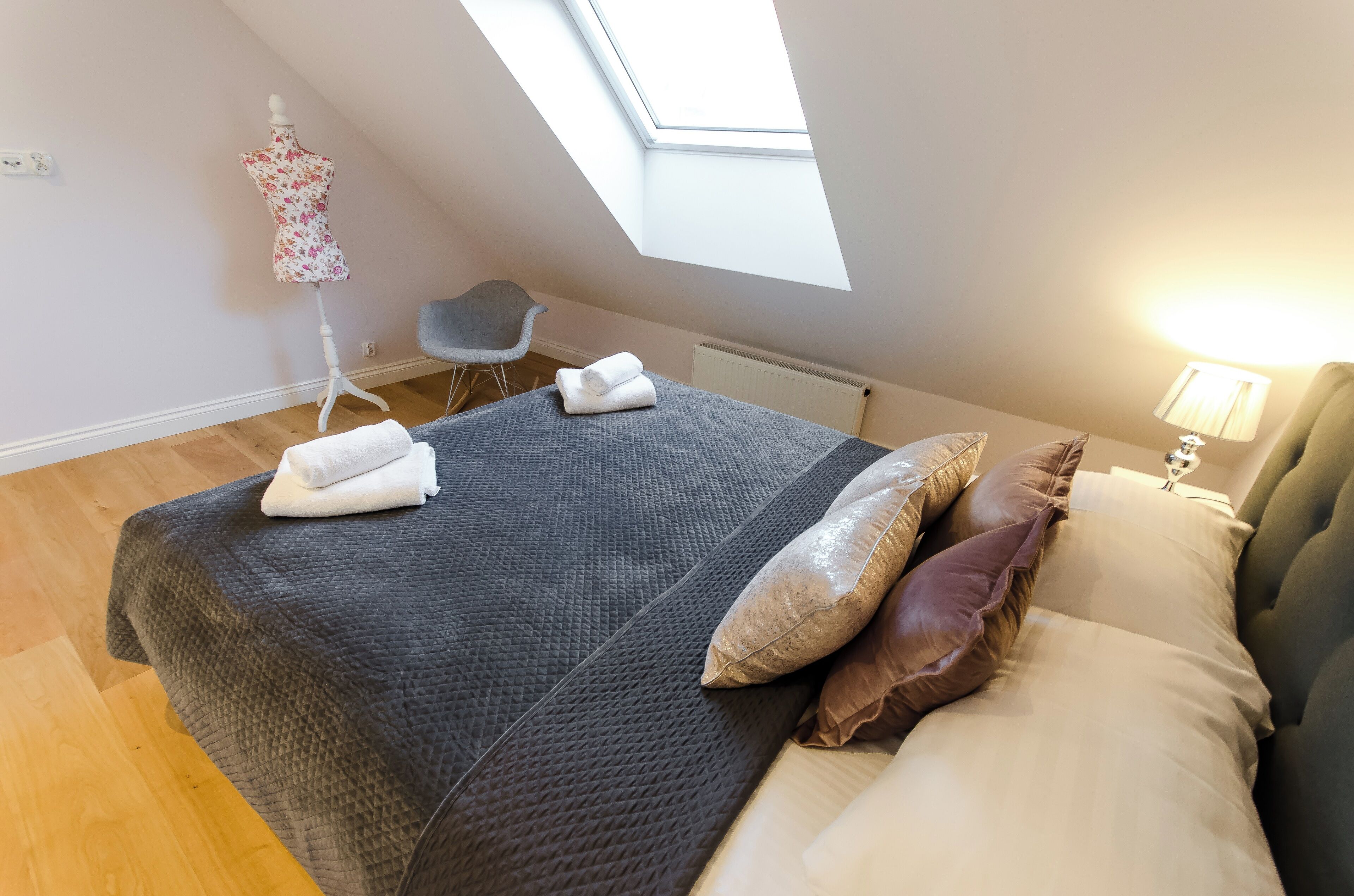 A bedroom with a bed, pillows, a chair, a radiator, and a skylight.