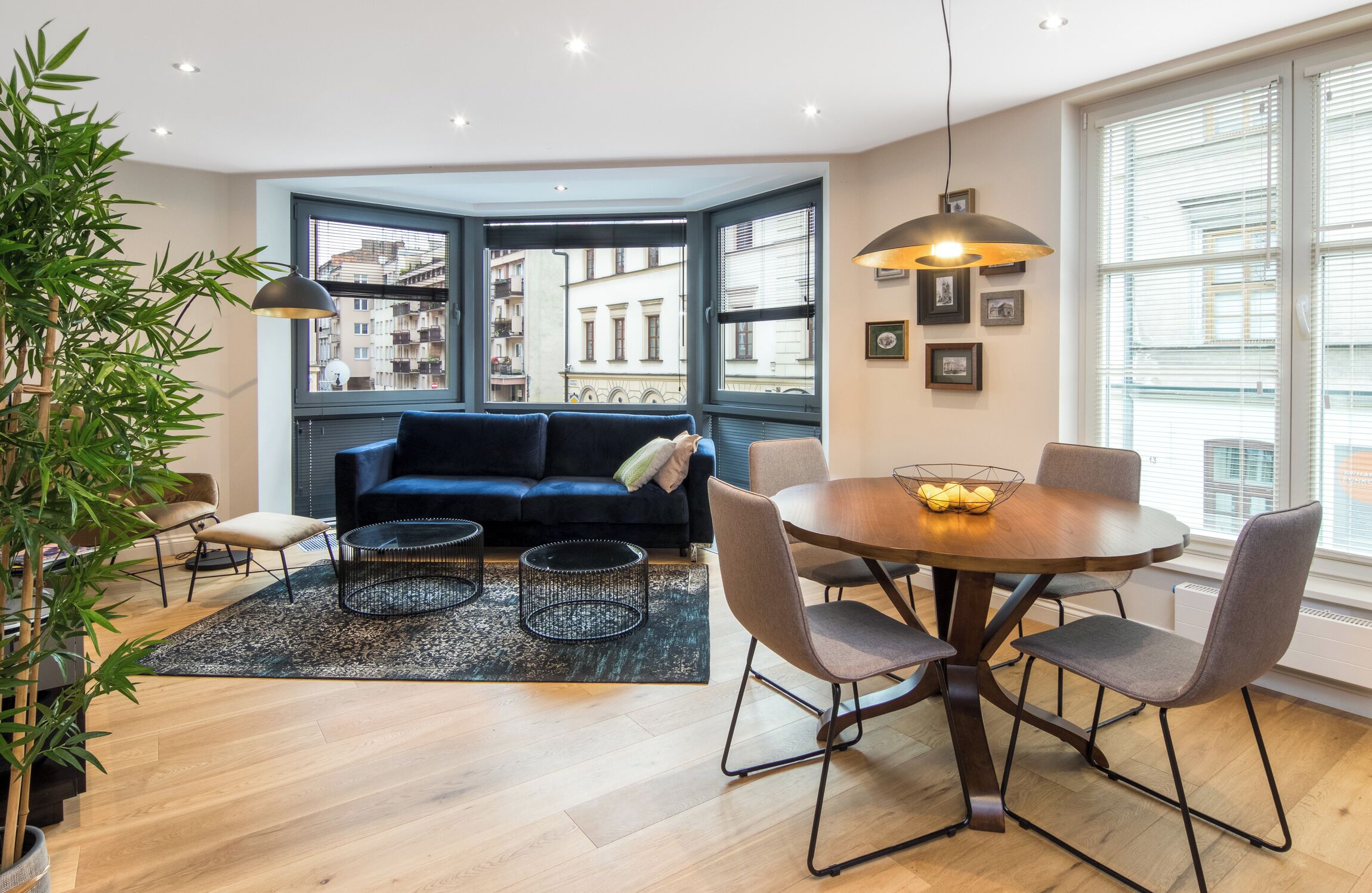 Ein modernes Wohnzimmer mit einem dunkelblauen Sofa, einem runden Esstisch mit Stühlen, einem kleinen Couchtisch und einem großen Fenster mit Blick auf die Stadt.