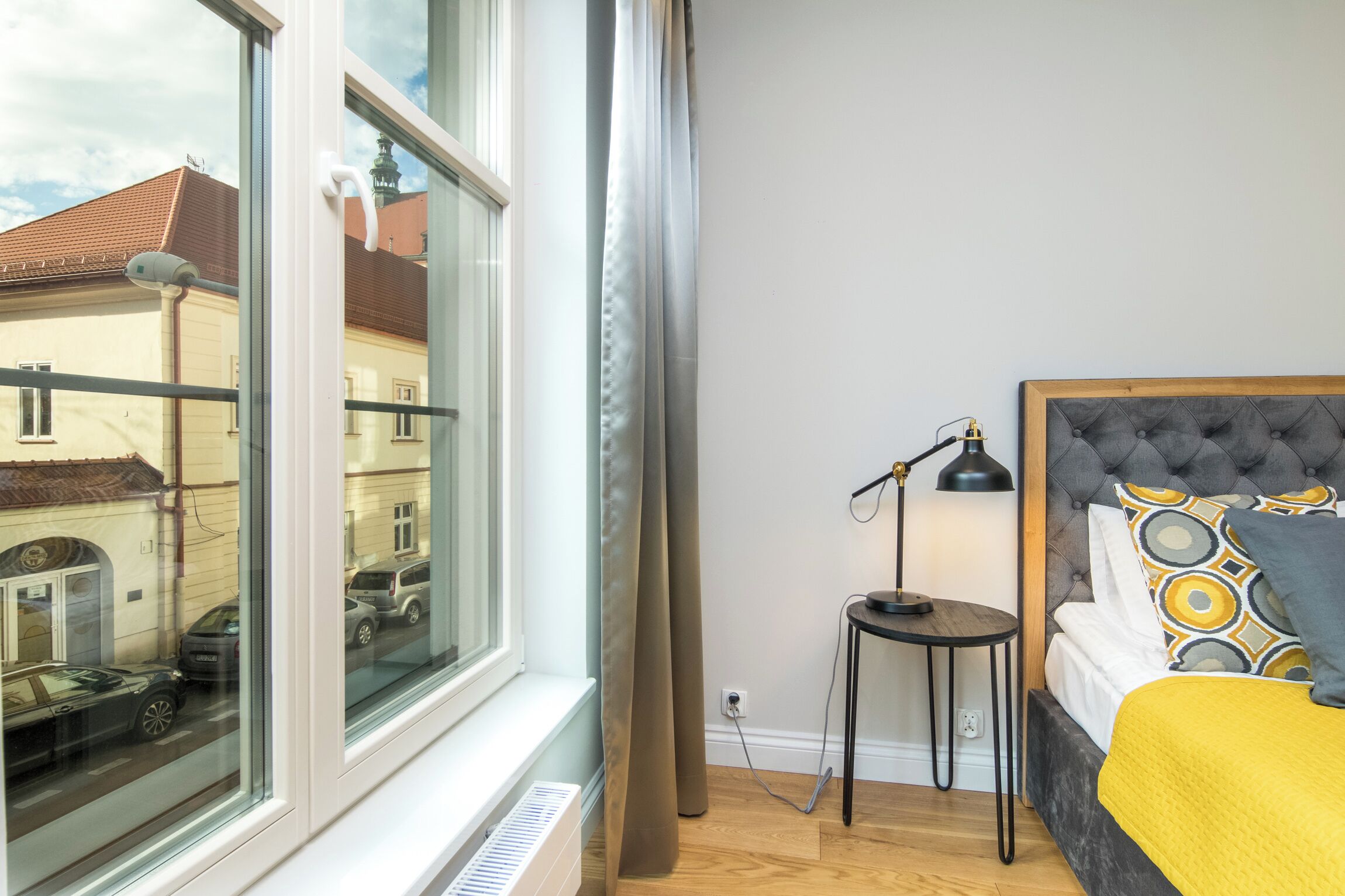 Un dormitorio con cama, una mesita de noche con lámpara, una ventana con cortinas y un radiador.
