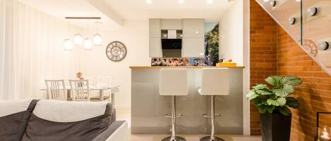 A modern living room with a sofa, dining table, and kitchen area with bar stools.