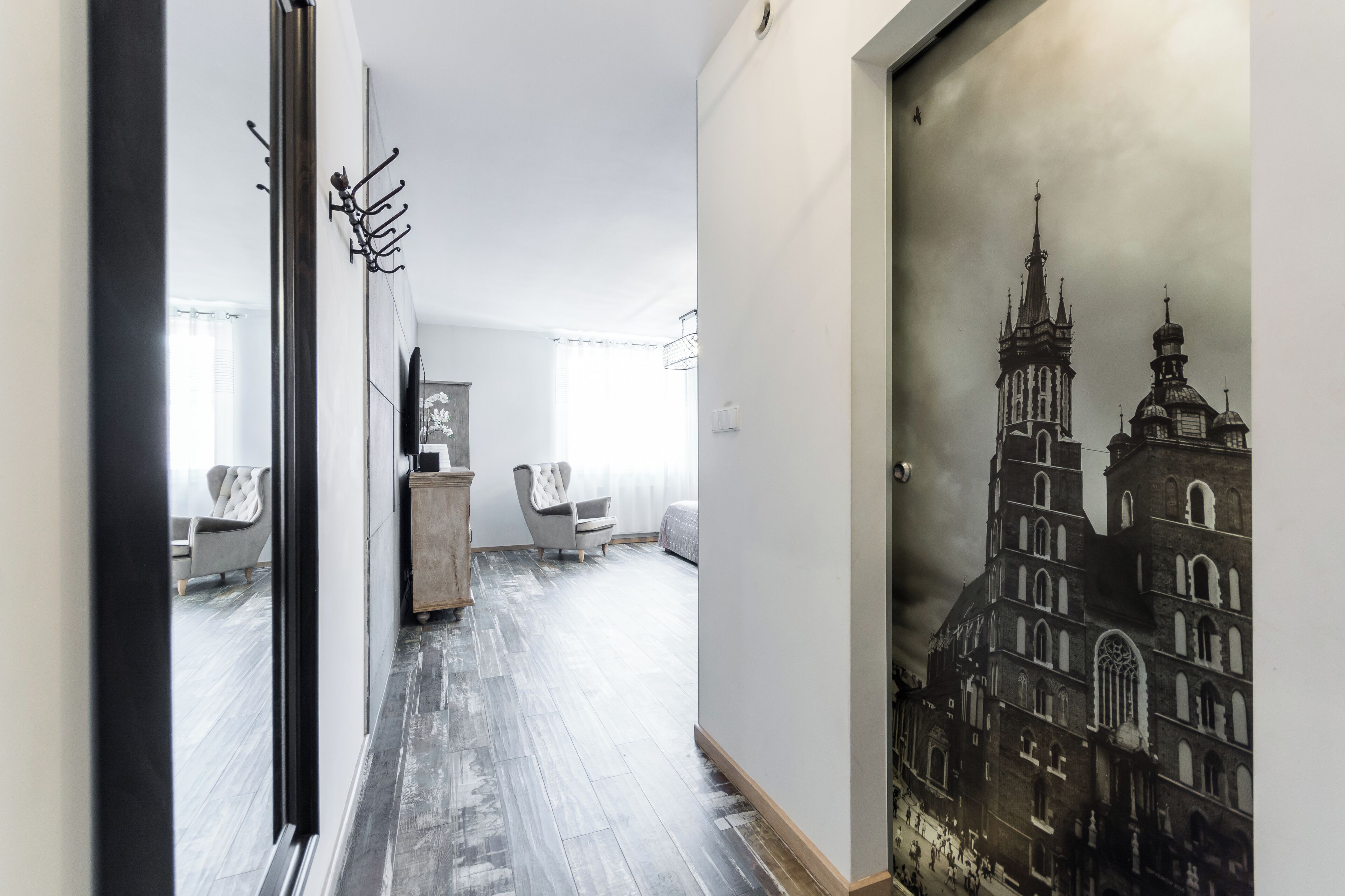 A hallway with a wooden floor, a coat rack, and a framed picture of a building.
