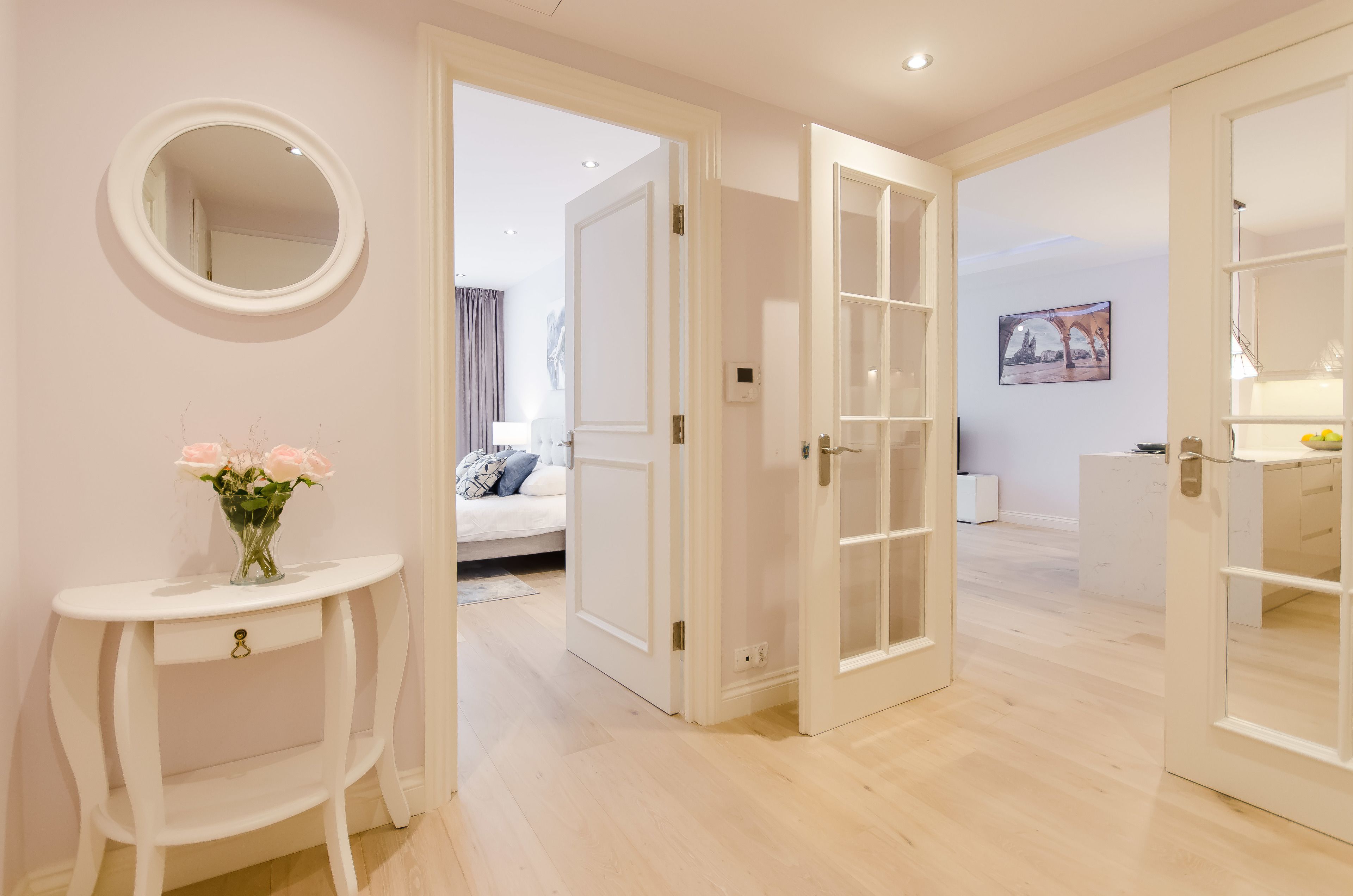 Ein modernes Hotelzimmer mit Bett, einem kleinen Tisch mit Blumenvase und einem großen Spiegel an der Wand.
