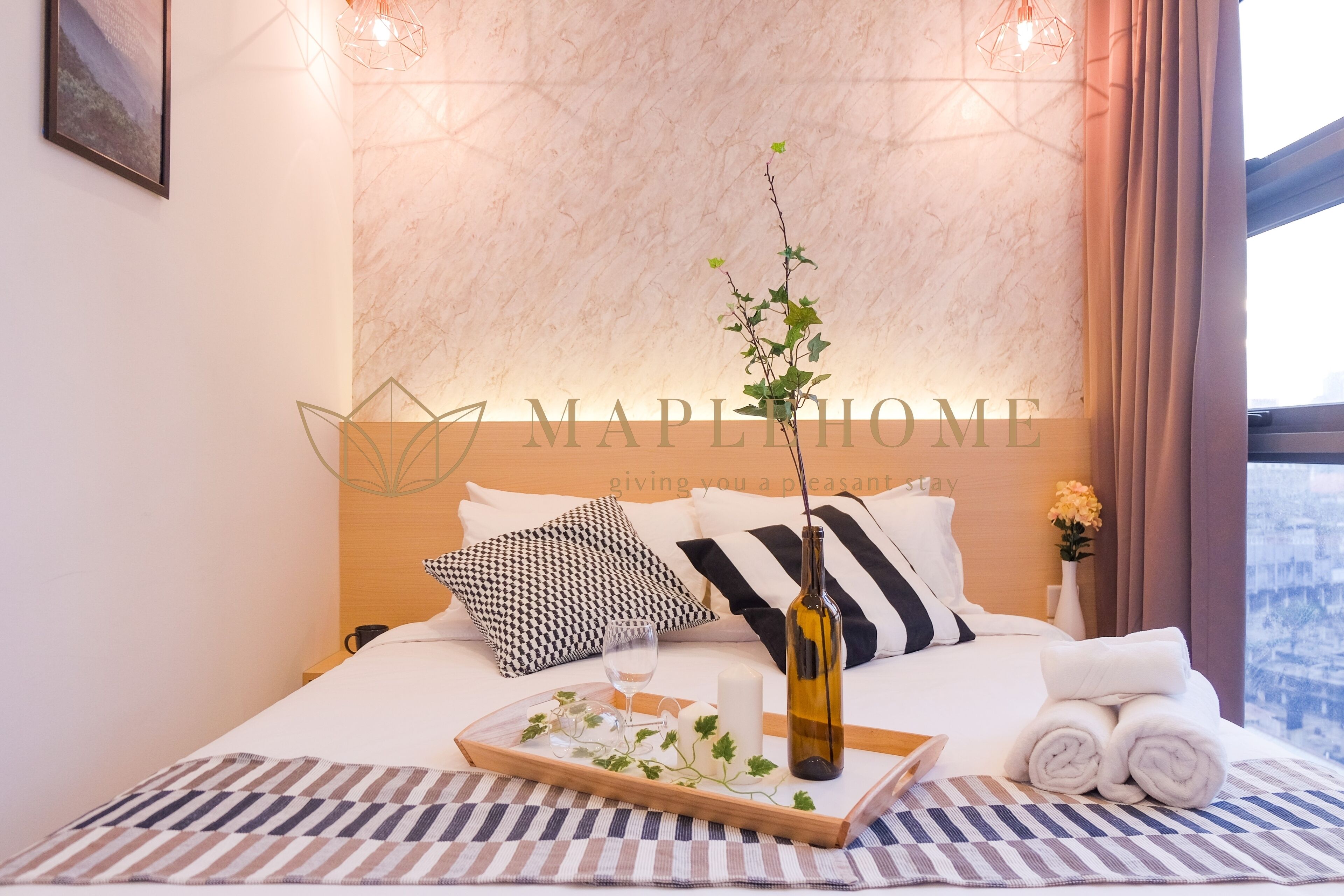 A neatly made bed with a tray of items, a bottle, and towels.