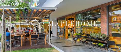 An outdoor seating area with tables and chairs, a fruit stand, and a restaurant entrance.
