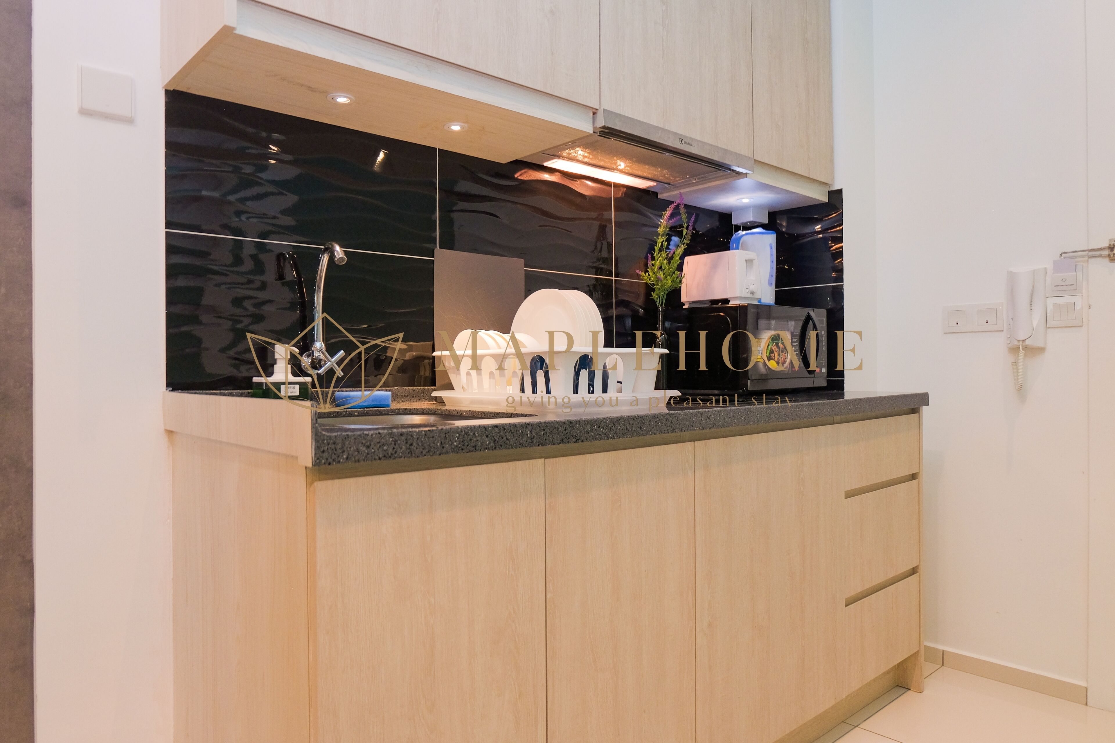 A modern kitchen with a black backsplash, wooden cabinets, and a countertop with a coffee machine and a plant.