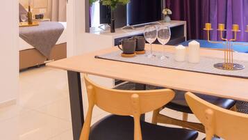 A dining area with a table set for two, a television in the background, and a sofa with cushions.