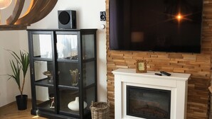 A modern living room with a wooden herringbone floor, a black glass cabinet, a white fireplace, and a mounted TV. - City Apartments Will (Emmerich)