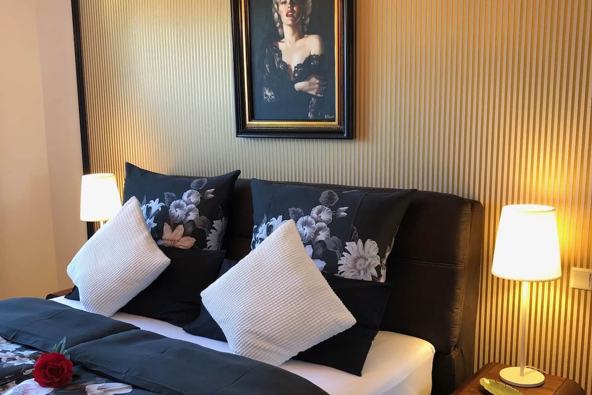 A neatly made bed with floral bedding, a framed portrait on the wall, and bedside lamps.