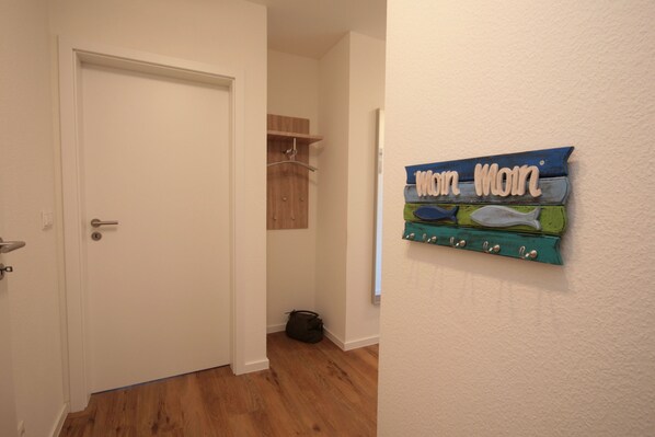A hallway with a white door, a coat rack, and a wall-mounted sign that reads "Walt Minn." - Quartier Hohe Geest 14 (Cuxhaven)