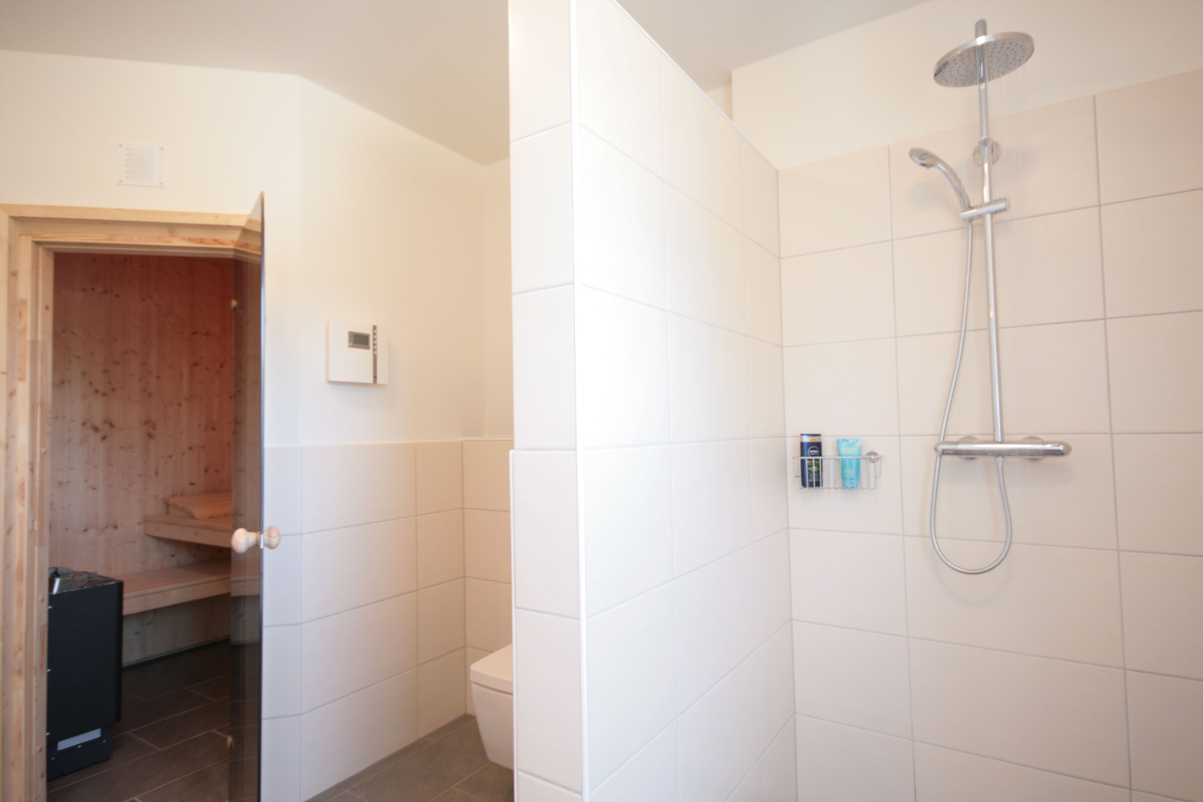 A bathroom with white tiles, a shower, and a toilet.