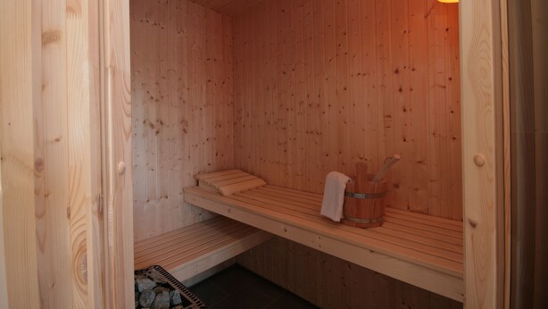 Een houten sauna met banken, een handdoekrek en een stenen kachel.