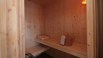 A wooden sauna with benches, a towel rack, and a stone heater.