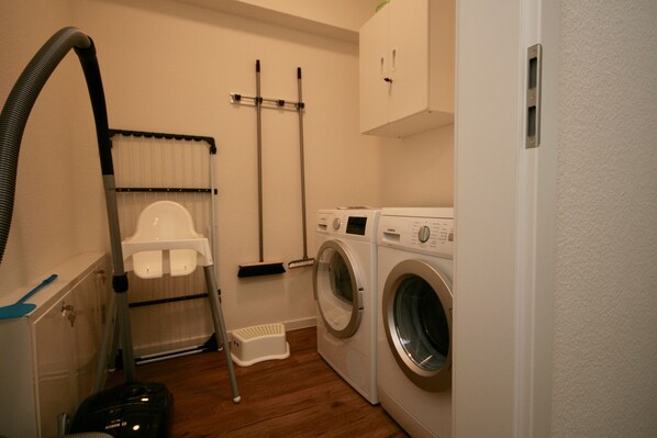 A laundry room with a washing machine, dryer, vacuum cleaner, and ironing board. - Quartier Hohe Geest 14 (Cuxhaven)
