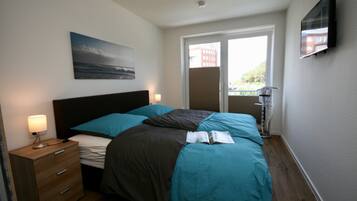 A bedroom with a bed, a nightstand, a lamp, a painting, and a TV on the wall.