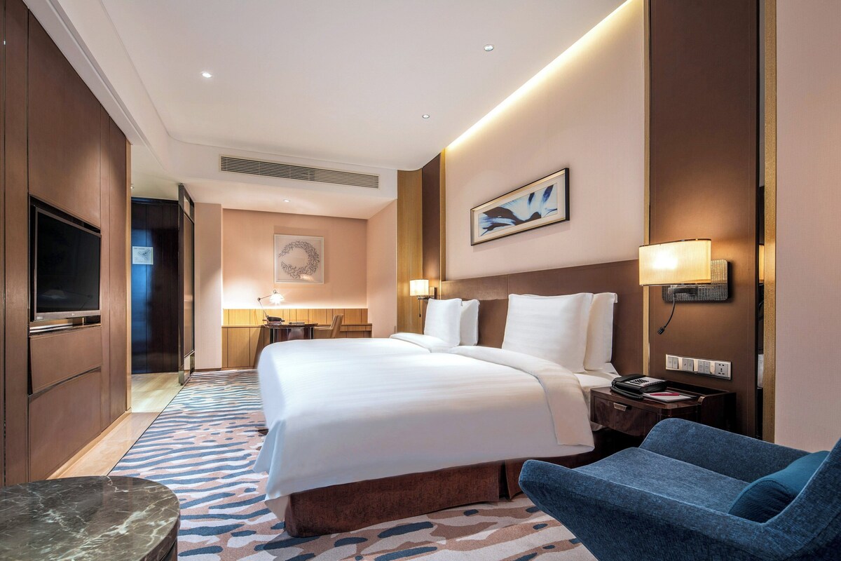 Een hotelkamer met een groot bed, een bureau, een stoel, een televisie en een schilderij aan de muur.