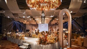 A stage with a large 'H' screen, surrounded by floral arrangements and a chandelier.
