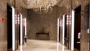 A modern lobby with a marble floor, a central table with a vase, and a ceiling with hanging lights.