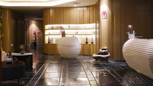 A modern lobby with a polished black floor, a central round white planter, and a reception desk with a unique design.
