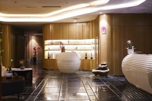 A modern lobby with a polished black floor, a central round white planter, and a reception desk with a unique design. - Crowne Plaza Dalian Sports Center by IHG (Dalian)