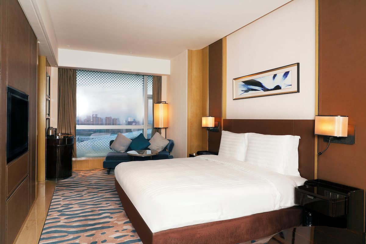 Ein Hotelzimmer mit einem großen Bett, einem Fernseher, einer Sitzecke mit Blick und einem Vorhangfenster.