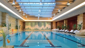 A large indoor swimming pool with multiple lounge chairs and potted plants.