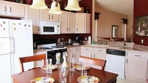 A kitchen with white cabinets, a stove, microwave, and a dining table set with plates and glasses.