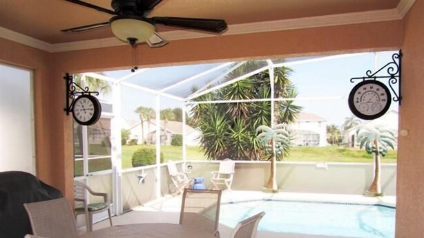 A covered patio with a pool, outdoor furniture, and two wall clocks.