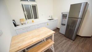 A kitchen with white cabinets, a stainless steel refrigerator, a wooden table, and a built-in sink. - ManMan House (New Taipei City)