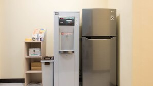 A compact kitchenette with a water dispenser, a refrigerator, and a small shelf unit with storage boxes. - ManMan House (New Taipei City)